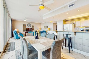 A dining area with a table, chairs, and a bar area with a refrigerator. - Gulf-view retreat with washer,dryer, AC, pool, sauna, & fitness center (Gulf Shores)
