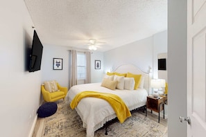 A bedroom with a bed, a yellow armchair, a bedside table with a lamp, and a wall-mounted TV. - 3rd-floor beachfront condo with pool, sauna, gym, hot tub, Gulf views, balcony (Gulf Shores)