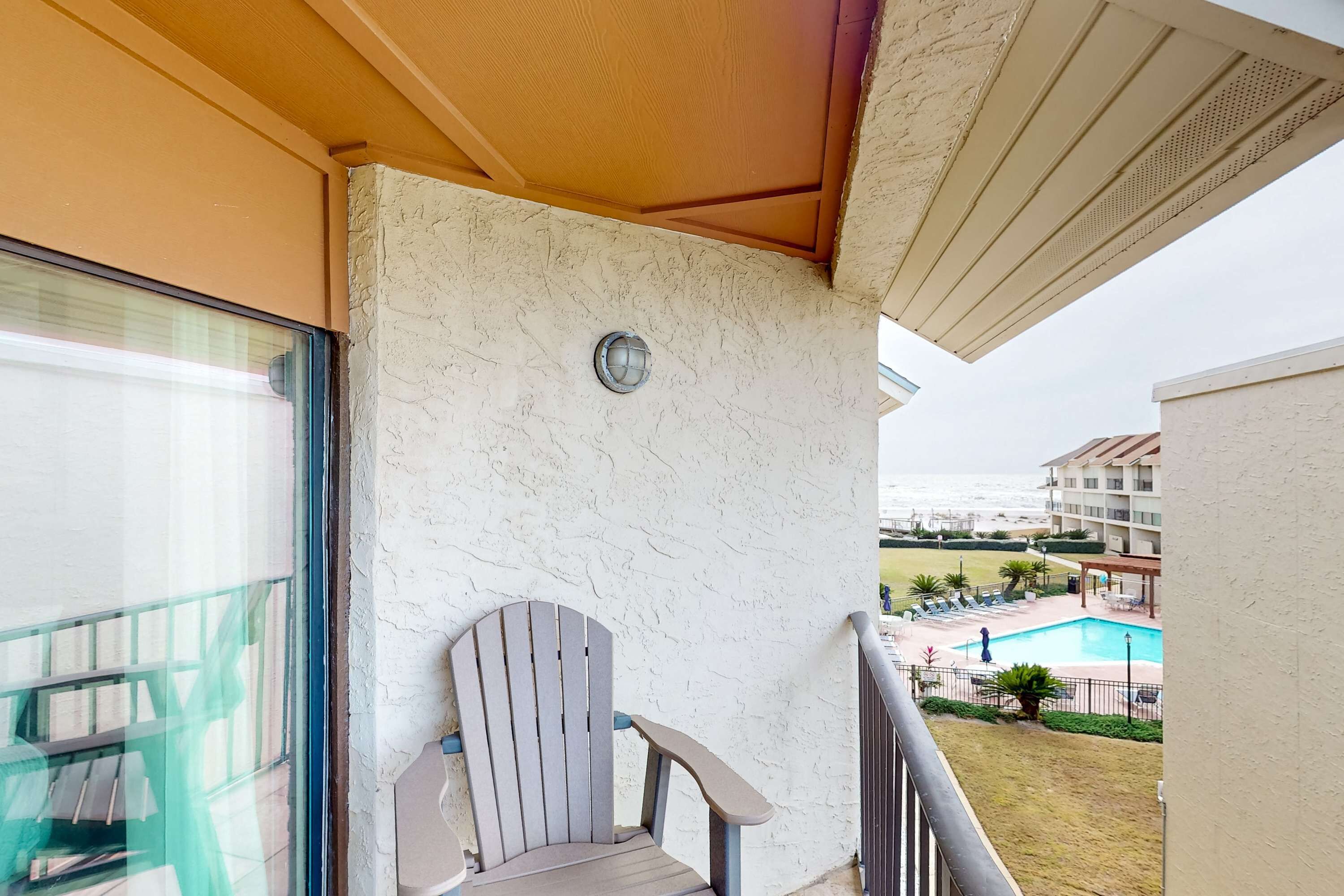 Ein Balkon mit einem Stuhl, einer Glastür und Blick auf einen Swimmingpool und Gebäude.