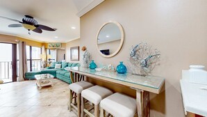 Un salon comprenant une table à manger avec un plateau en verre, un ventilateur de plafond, un canapé et un grand miroir.