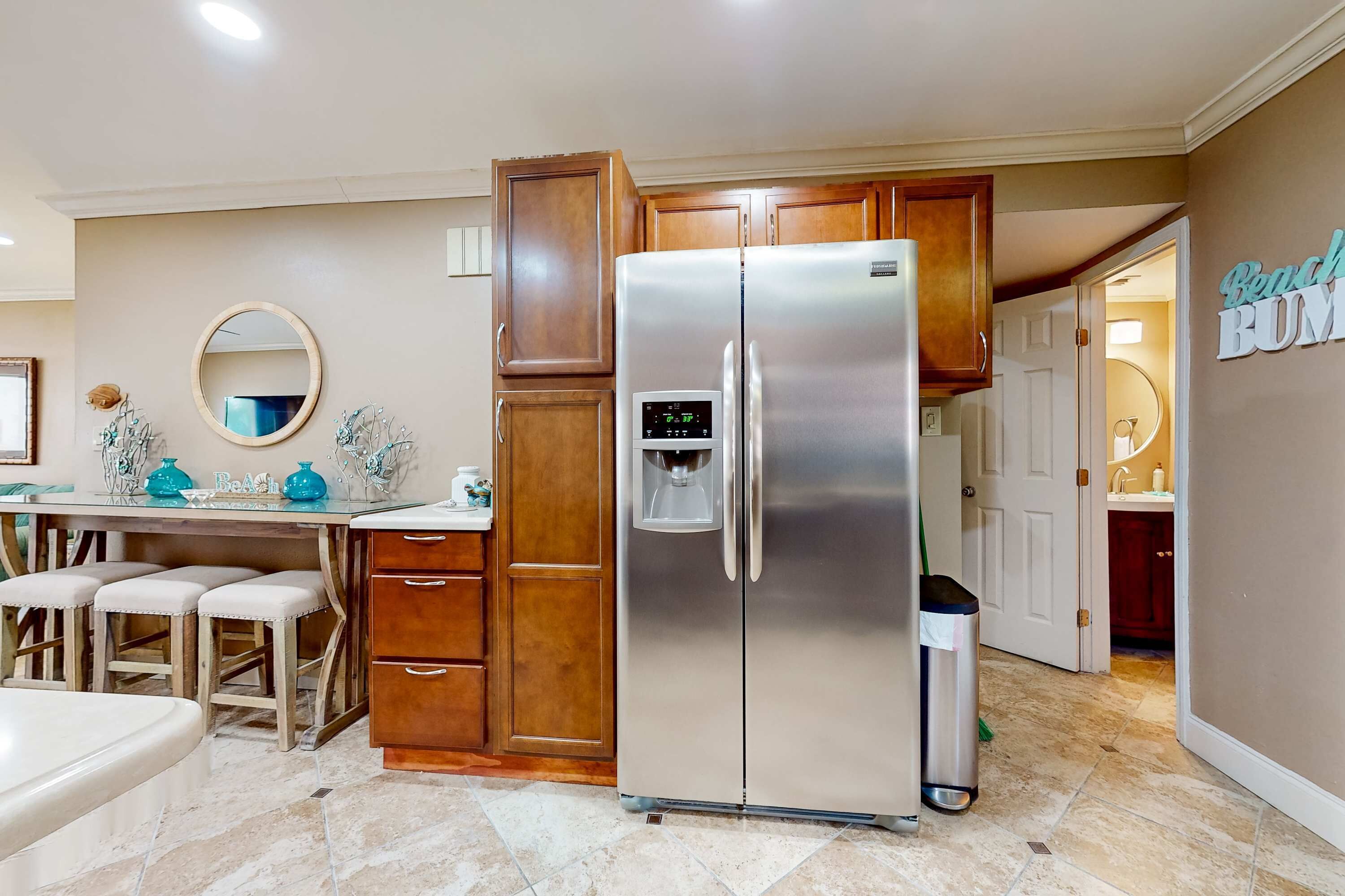 Una cocina con refrigerador de acero inoxidable, armarios de madera, una barra con taburetes y un letrero en la pared.