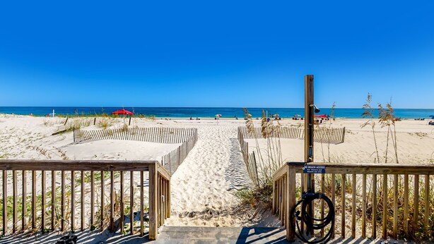Une plage avec une barrière en bois, un panneau indiquant l’interdiction d’accès à la plage et une vue dégagée sur l’océan.