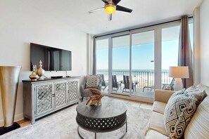 A modern living room with a flat-screen TV, a round coffee table, a sofa, and a balcony with a view. - Gulf-Front Condo on the Beach w Balcony & Shared Pools, Hot Tubs, Sauna & Gym (Gulf Shores)