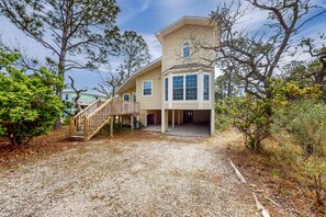 A two-story house with a covered porch, a wooden staircase, and a gravel driveway. - Sunny coastal hideaway with patio, large deck, W&D, & central AC (Gulf Shores)