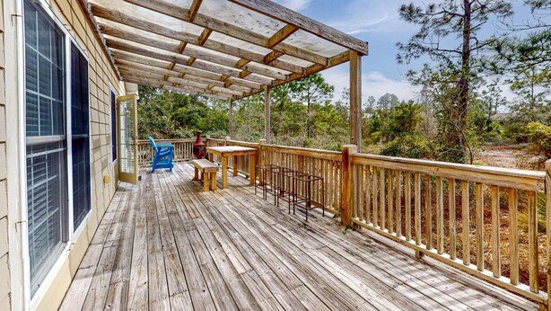 Un terrazzo in legno con una pergola, mobili da esterno e vista sugli alberi.