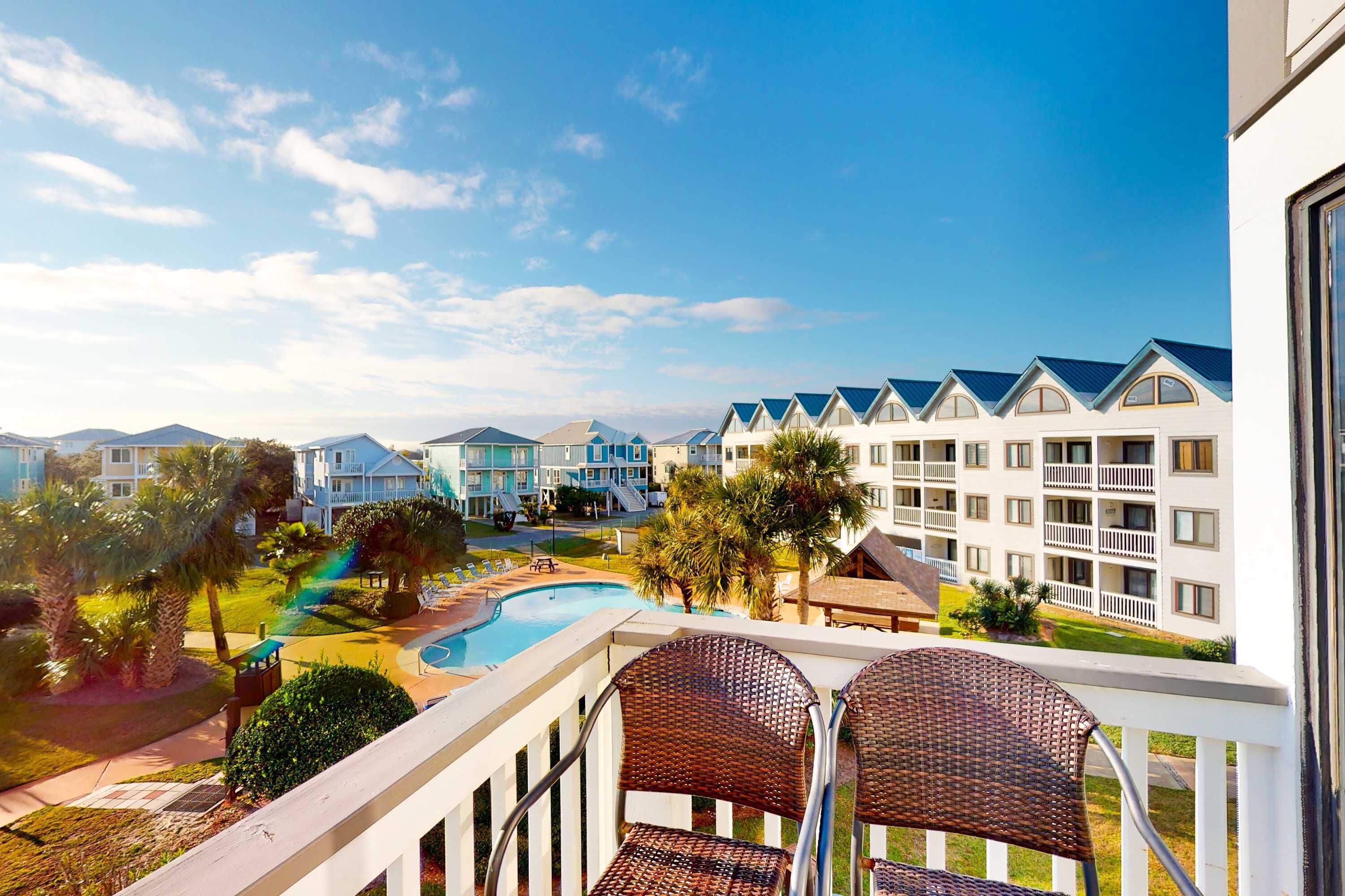 A hotel balcony with wicker chairs, a swimming pool, and a view of other hotel buildings.