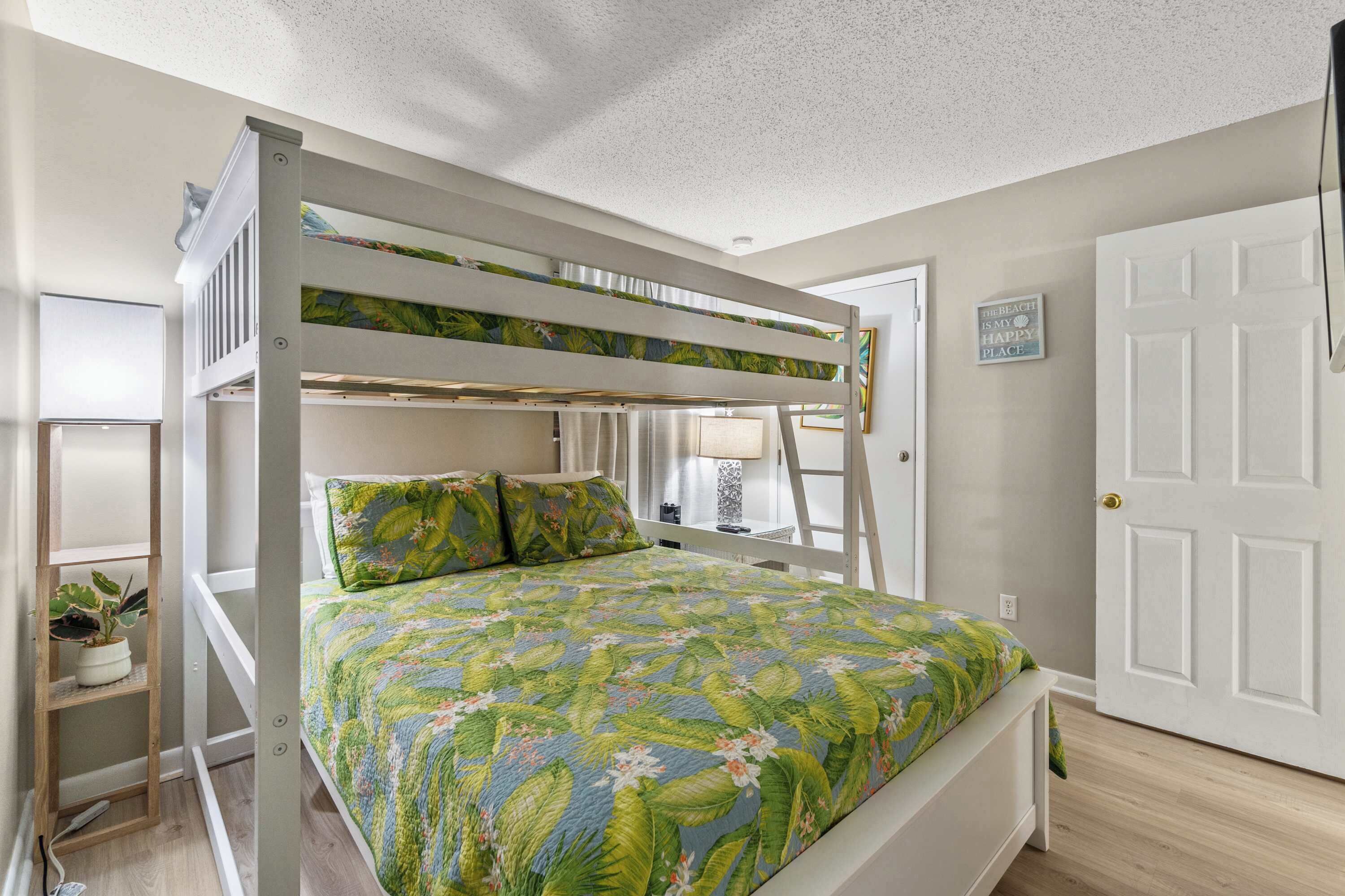 A bunk bed with a floral bedspread, a white door, and a small plant on a shelf.