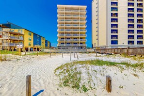 A beachfront hotel with multiple floors, a sandy beach in the foreground, and a wooden boardwalk. - Unique dog-friendly Gulf-front condo with amazing views, pools, sauna, gym, & AC (Gulf Shores)