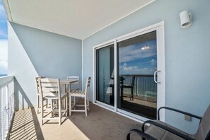 Een balkon met een tafel en stoelen, een schuifpui en uitzicht op zee.