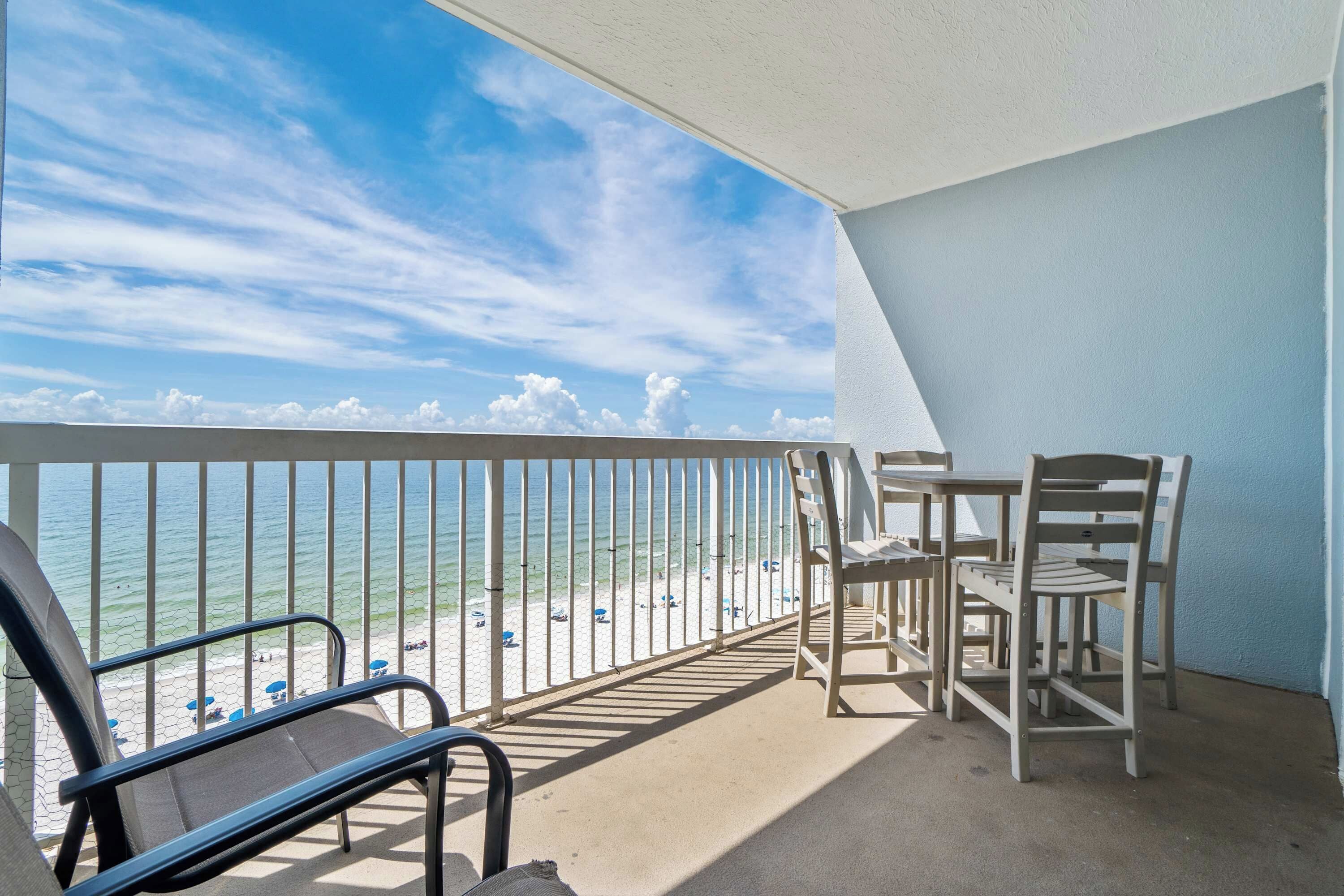 A balcony with a view of the beach, a table, and two chairs.