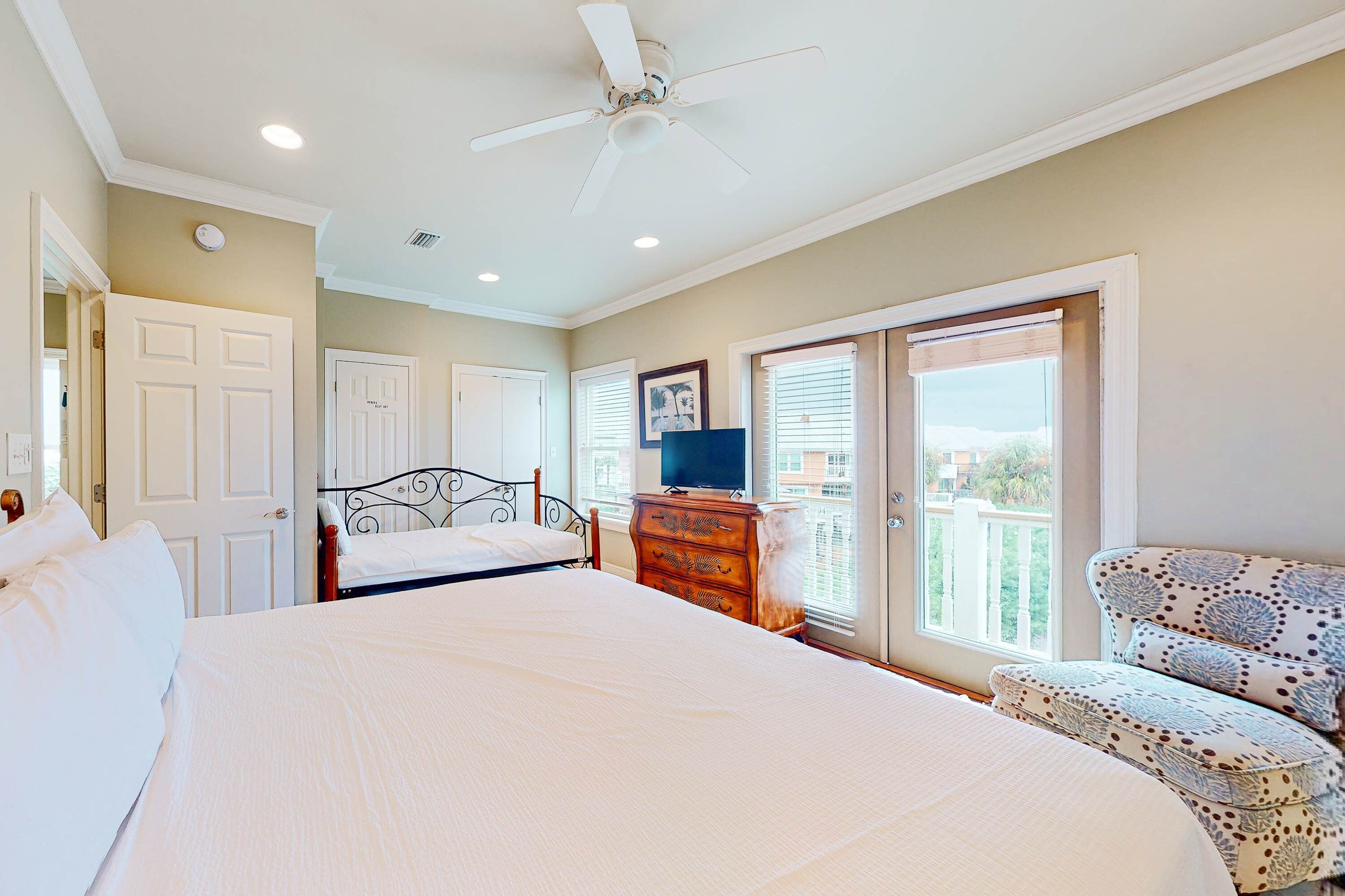 A bedroom with a large bed, a dresser, a television, and a balcony with a view.