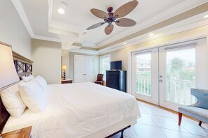 Ein Schlafzimmer mit Bett, Deckenventilator, Fernseher, Stuhl und einem Balkon mit Aussicht.