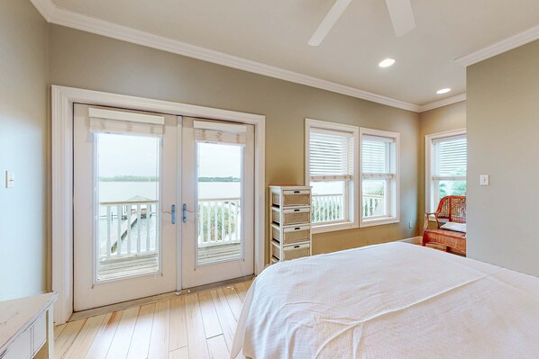 Ein Schlafzimmer mit einem großen Bett, einer Glastür zum Balkon und Blick ins Freie.
