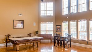 A spacious room with a pool table, a dining table with chairs, large windows, and a framed picture on the wall. - Delightful coastal gem with pool, hot tub, private balcony, fast WiFi & AC (Gulf Shores)