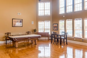 A spacious room with a pool table, a dining table with chairs, large windows, and a framed picture on the wall. - Delightful coastal gem with pool, hot tub, private balcony, fast WiFi & AC (Gulf Shores)