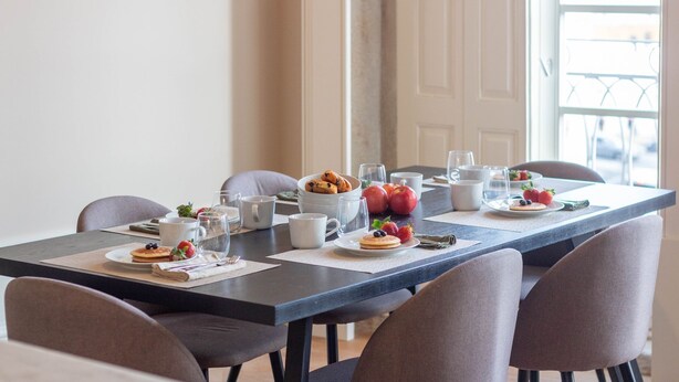 A dining table set with breakfast items, including pastries, fruits, and beverages, in a room with a view. - LovelyStay - Entreparedes House - 302 (Porto)