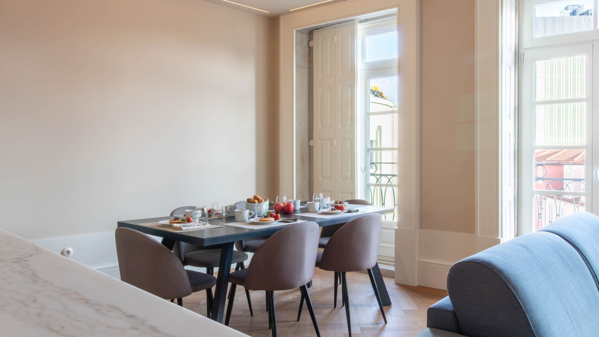 Uma sala de jantar com mesa posta para quatro, cadeiras e vista para uma varanda.