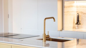 A modern kitchen with a gold faucet, a marble countertop, and a sleek backsplash. - LovelyStay - Entreparedes House - 302 (Porto)