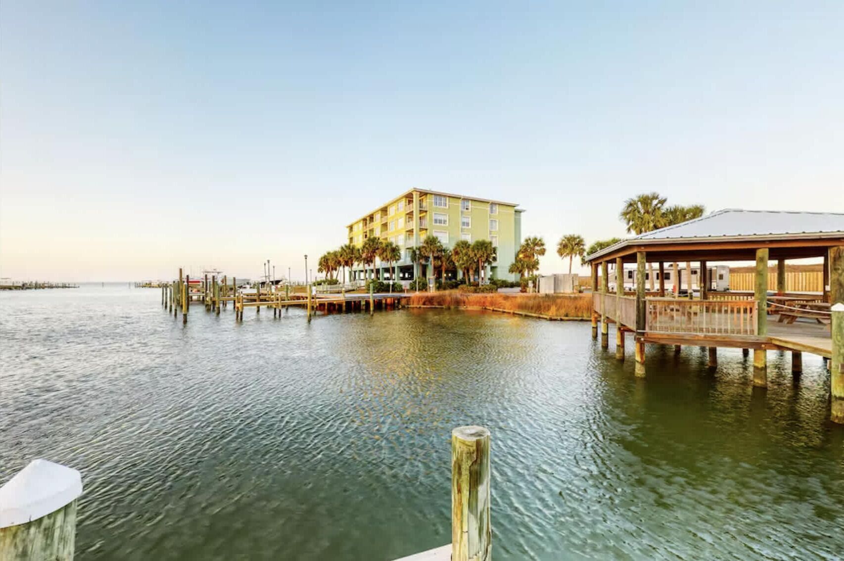 Un hotel frente al agua con un muelle, un pabellón cubierto y un edificio con varios balcones.