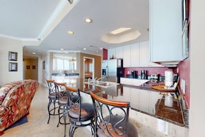 A kitchen with a central island, bar stools, a refrigerator, and a microwave. - Gulf-view condo with direct beach access, indoor & outdoor pools, hot tub, sauna (Gulf Shores)
