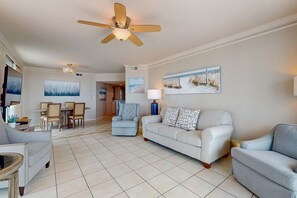 Ein Wohnzimmer mit Deckenventilator, einer Couch, einem Sessel, einem Esstisch mit Stühlen und Bildern an den Wänden.