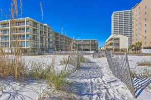 Ein Hotel direkt am Strand mit mehreren Etagen, einem Sandstrand davor und einem strahlend blauen Himmel.