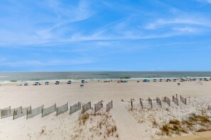 A beach with a wooden fence, umbrellas, and people. - Beachfront condo with Gulf views, balcony, pool & AC - snowbird-friendly (Gulf Shores)