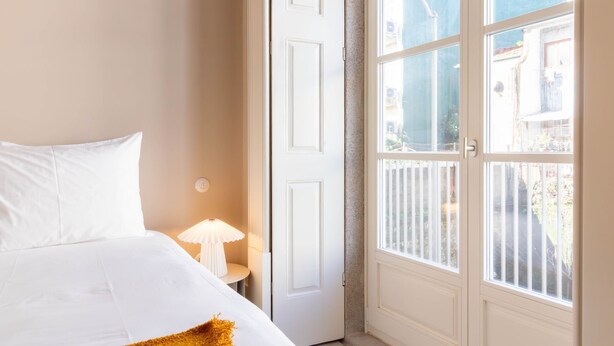 Hotellihuone, jossa on sänky, yöpöytä lampun kanssa ja suuri ikkuna, josta on näkymä ulos.