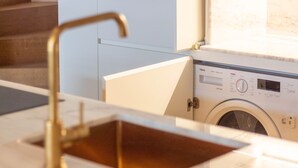Moderni keittiö, jossa on sisäänrakennettu pesukone, ruostumattomasta teräksestä valmistettu allas ja vaaleanvärinen työtaso.