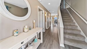 A hallway with a staircase, a round mirror, a console table with decorative items, and a light-colored wall. - Remodeled, lagoon-front home with decks, views, paddleboat (Gulf Shores)