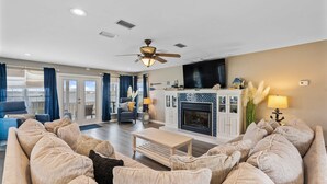 A living room with a sofa set, a fireplace, a ceiling fan, and a television. - Remodeled, lagoon-front home with decks, views, paddleboat (Gulf Shores)