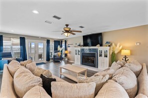 A living room with a sofa set, a fireplace, a ceiling fan, and a television. - Remodeled, lagoon-front home with decks, views, paddleboat (Gulf Shores)
