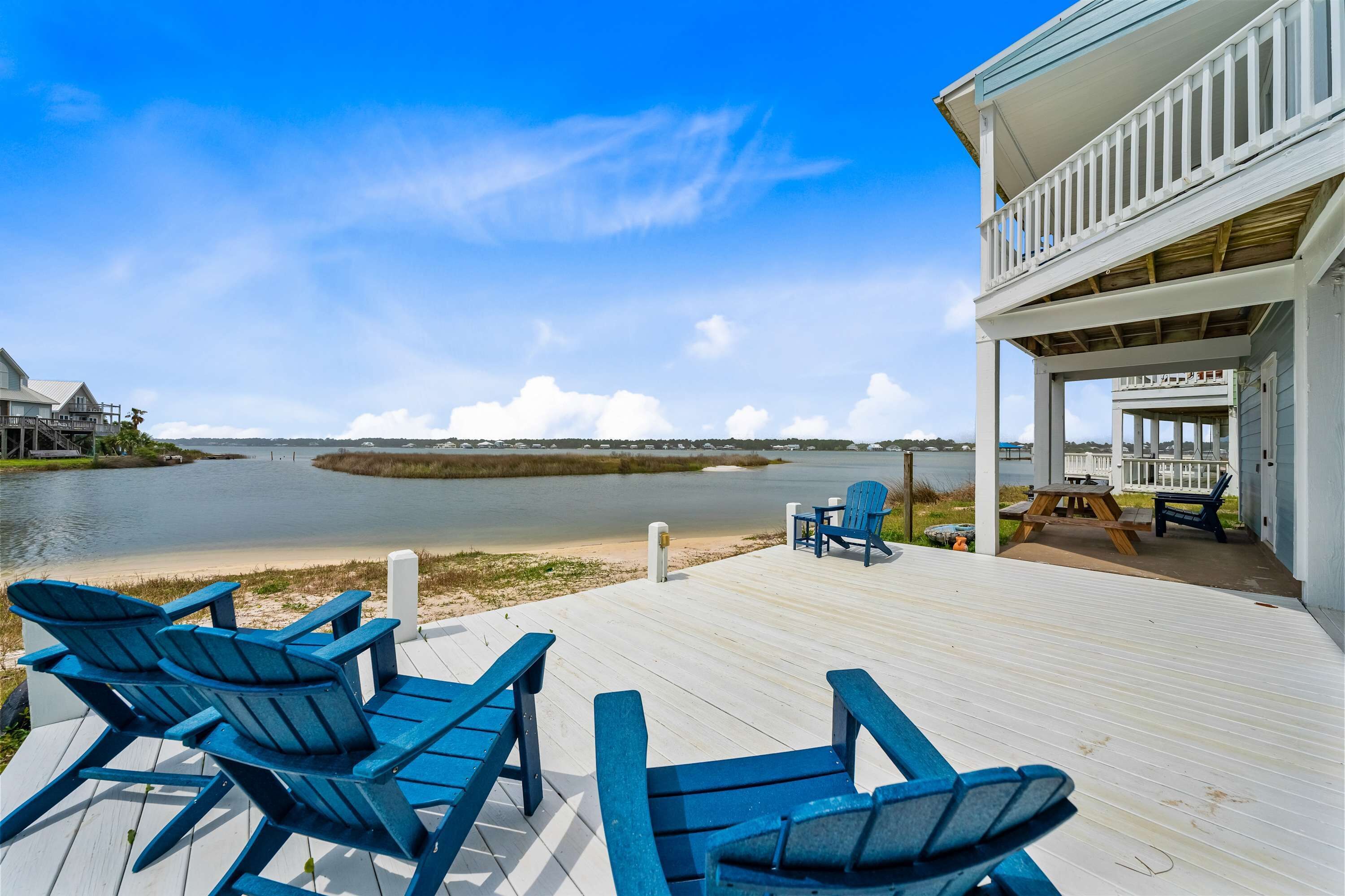 Een houten terras met blauwe Adirondack-stoelen en uitzicht op een rustig meer.