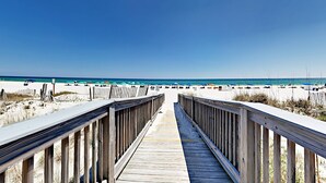 Una passerella in legno conduce a una spiaggia con ombrelloni e bagnanti.