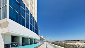 Un edificio moderno con ampie finestre, una zona piscina e vista sulla spiaggia.