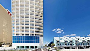 Un hotel moderno con un edificio alto e cilindrico, situato su una spiaggia e caratterizzato da edifici di colore azzurro chiaro.