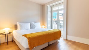 Ein Hotelzimmer mit einem großen Bett, zwei Nachttischen, einem Fenster mit Blick auf Gebäude und einem Holzboden.
