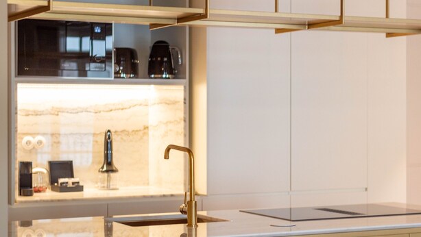 Eine moderne Küche mit Spüle aus Edelstahl, Armatur aus Gold und einer Marmor-Spritzschutzwand.