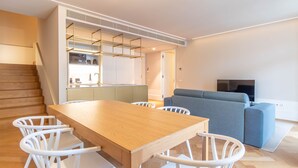 Ein zeitgemäßer Wohnraum mit einem Holzessttisch, weißen Stühlen, einem grauen Sofa und einem Fernseher.