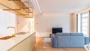 Ein modernes Wohnzimmer mit einer Couch, einem Fernseher und einer Küchenzeile mit Spüle und Arbeitsplatte.