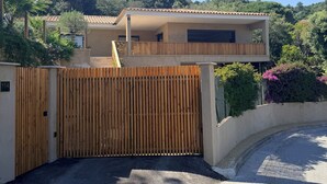 A modern house with a wooden gate, a covered patio, and a view of a hill with trees. - Villa and pool Pacha Prestige (Roquebrune-sur-Argens)