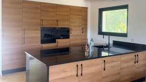 A modern kitchen with wooden cabinets, a black countertop, and a window with a view. - Villa and pool Pacha Prestige (Roquebrune-sur-Argens)