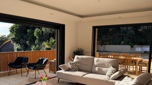 A modern living room with a large sofa, a coffee table, and a dining area with wooden furniture. - Villa and pool Pacha Prestige (Roquebrune-sur-Argens)