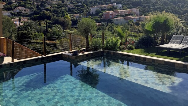 A clear view of a swimming pool with a checkered pattern, surrounded by greenery and overlooking a hillside with buildings. - Villa and pool Pacha Prestige (Roquebrune-sur-Argens)