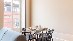 Uma sala de jantar com uma mesa redonda, cadeiras pretas e vista para um edifício através de uma janela.