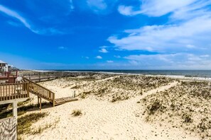 A beach with a wooden boardwalk leading to a building with a red railing. - Beachfront Home with Covered Deck, Gulf Views, Central AC, WiFi & Laundry (Gulf Shores)