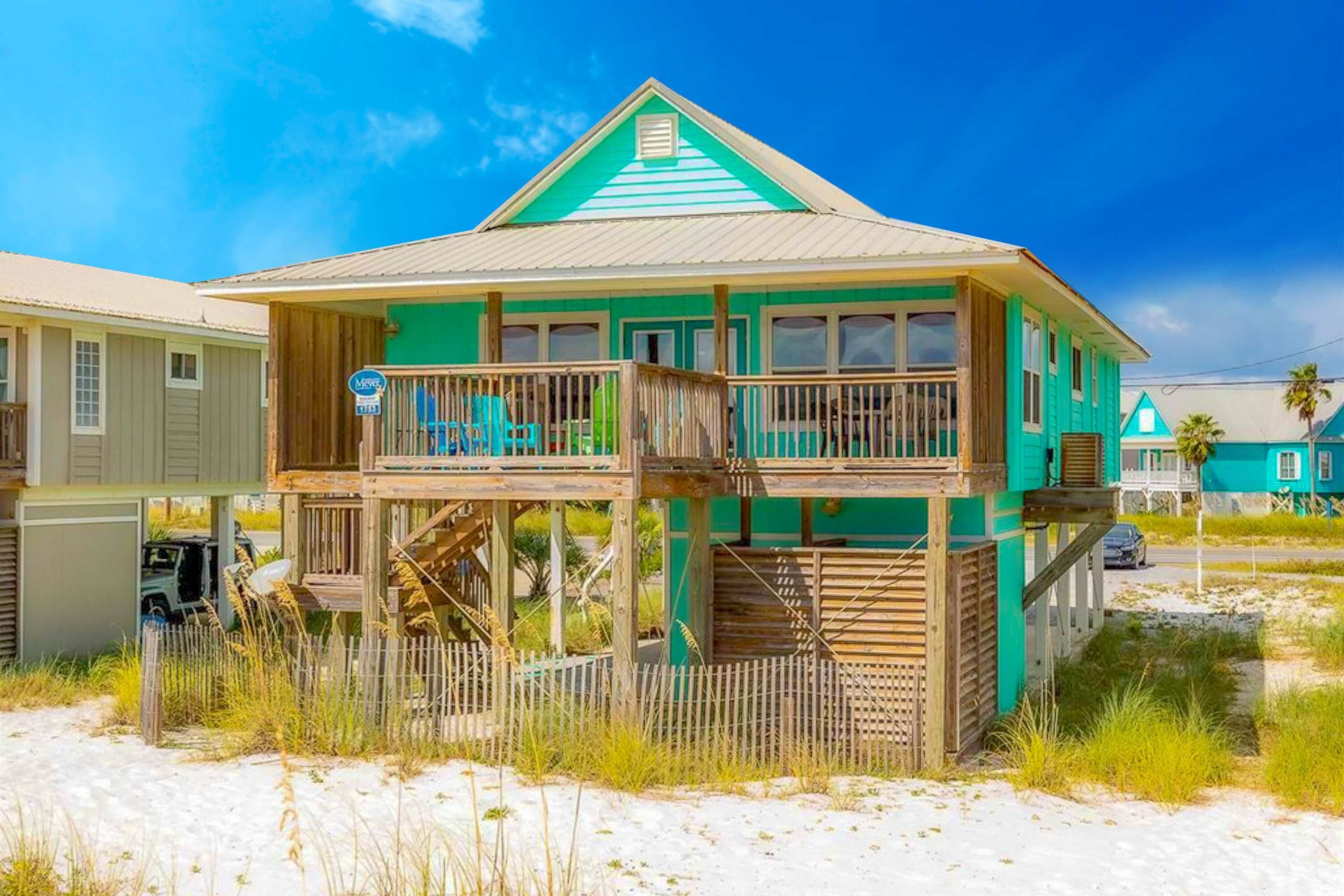 A two-story beach house with a balcony, a wooden deck, and a staircase leading to the upper level.