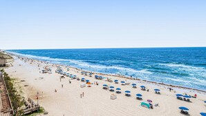 A beach with umbrellas, sun loungers, and a flag. - Gulf-Front, 12th-Floor Condo w Great View, Balcony, AC & Shared Pools Hot Tubs (Gulf Shores)