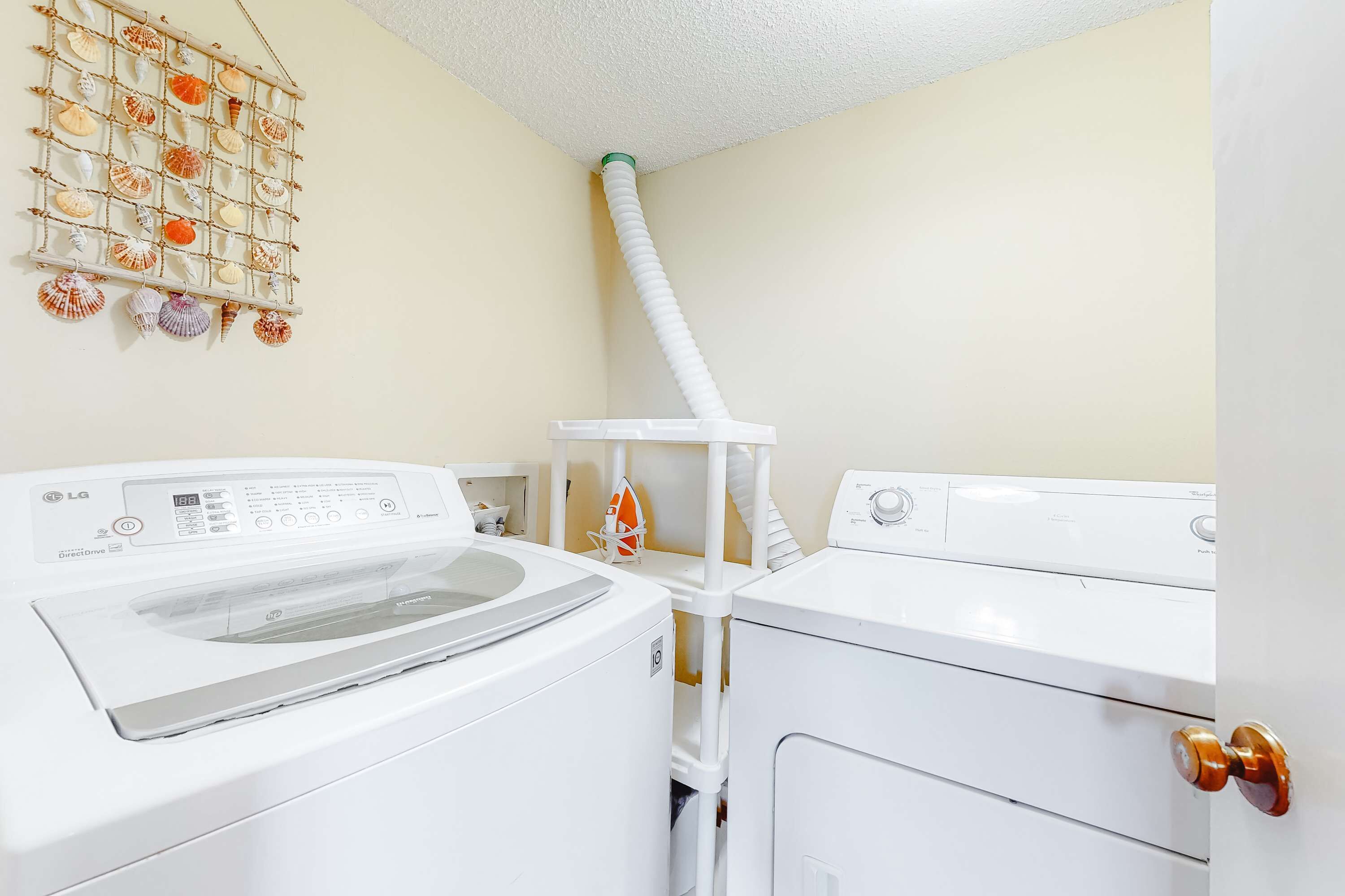 Une buanderie avec deux machines à laver blanches, un étendoir sur lequel sont disposés divers coquillages, et un tuyau d’arrosage blanc.