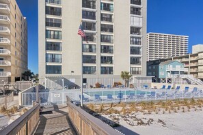 Ein mehrstöckiges Hotel mit Balkonen, einem Poolbereich mit Liegestühlen und Blick auf den Strand.